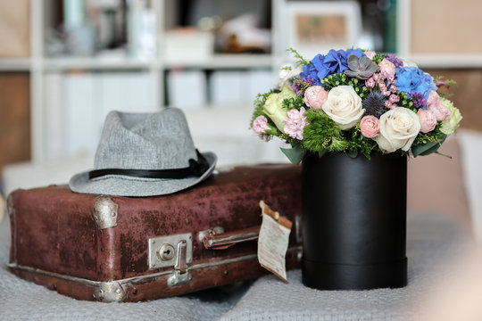 Mixed flowers in the box on the bed with suitcase and a hat