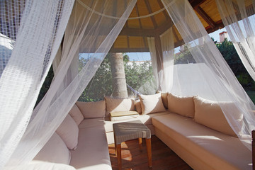 Luxury modern gazebo with soft furniture and curtains inside garden surrounded with palms