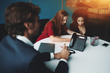 Scene in meeting room: two businesswomen (caucasian and Brazilian) and one man employer are sitting...