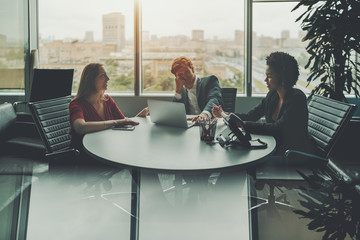 Meeting of three businesspeople in luxury office room near window: group of three co-workers of...
