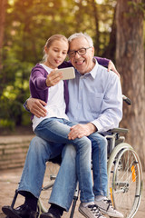 funny granddaughter using phone for selfie with her disabled father in wheelchair and mother.