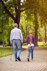 Obraz premium Girl and her disabled grandfather holding hands on walk.