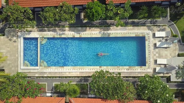 AERIAL TOP DOWN: Unrecognizable woman on summer vacation refreshing and swimming underwater in clear pool water on hot sunny day. Girl in pink bikini enjoying swimming in empty pool at luxury resort