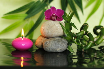 Fototapeta na wymiar galets disposés en mode de vie zen au centre avec une orchidée au sommet avec des tiges de bambou et une bougie rose allumée 
