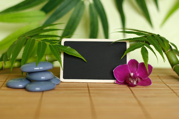 Galets gris disposés en mode de vie zen avec une orchidée,une bougie allumée ,un branche de bambou et des feuillages et une ardoise à message vide