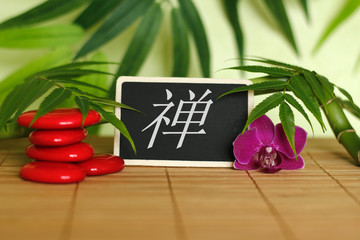 Galets rouge disposés en mode de vie zen avec une orchidée,une bougie allumée ,un branche de bambou et des feuillages avec le message zen en japonais sur l'ardoise