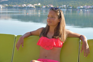 Young girl in bikini sitting in bar on seating chair overlooking the sea