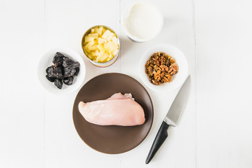 Ingredients for salad: chicken, walnuts, prunes, pineapple and sour cream on a white table with a knife