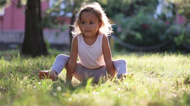 Little cute baby girl doing yoga exercise on the grass in park.