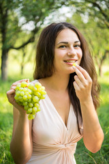 Beautiful girl tasting grapes in the garden