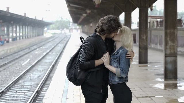 Romantic couple kissing and hugging in train station on rainy day before separation