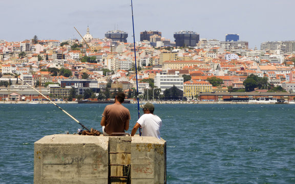 Two men fishing in river Tagus - Lisbon's cityscape in the background