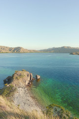 View from the top of a mountain at Gili Lawa overlooking other mountains at the coast with blue turquoise colored ocean water in between in Flores, Indonesia. © Eduard