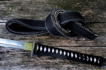 Black belt of martial arts and Japanese katana sword on old boards.