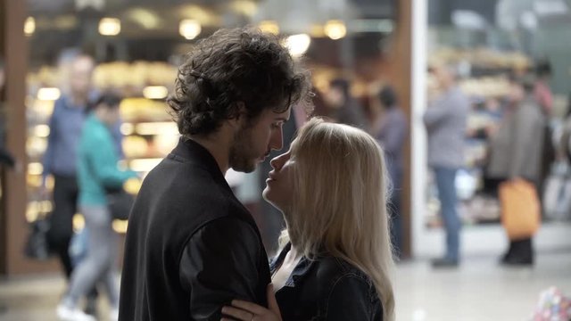 Young loving couple in kissing and talking in public on a street with people in background