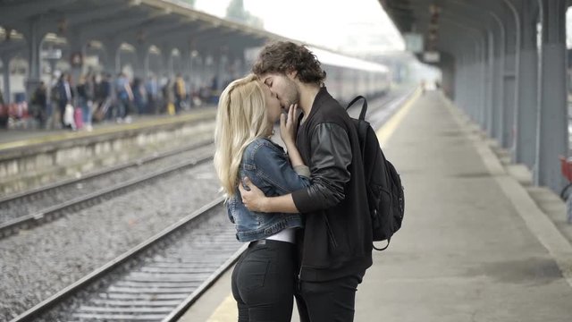 Young man kissing and saying and waving goodbye to his girlfriend in train station before leaving