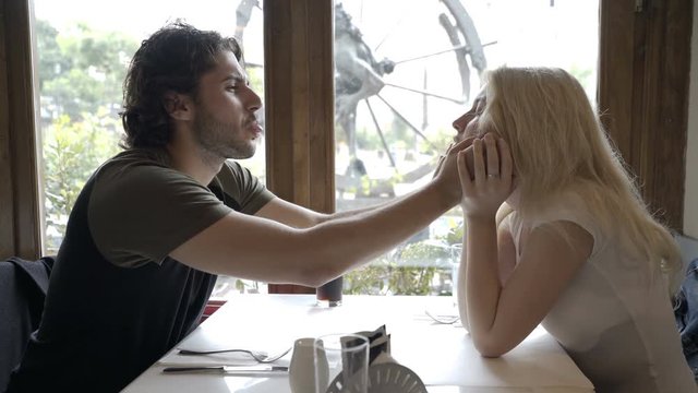 Couple in love making funny faces at each other sitting at dinner and waiting for order in restaurant