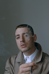 A handsome and lonely guy in a cloak with a cigarette