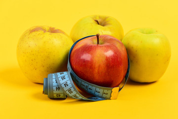 Tape for measuring and colorful apples on yellow background