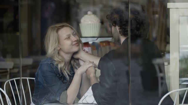 Closeup of romantic lovers sitting at the table of confectionery talking and caressing