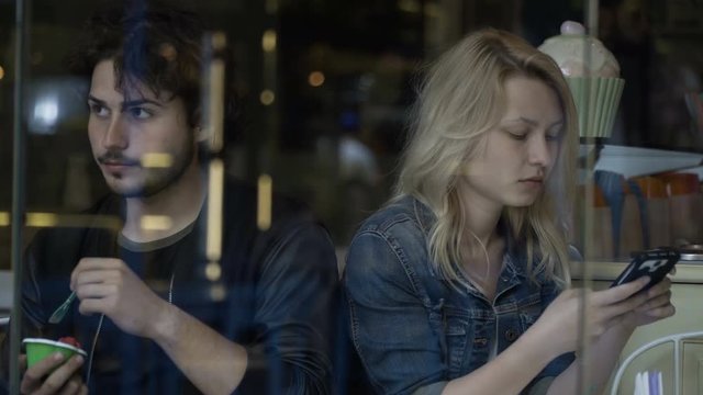 Sad boyfriend and distant upset girlfriend playing on smartphone having relationship problems and difficulties