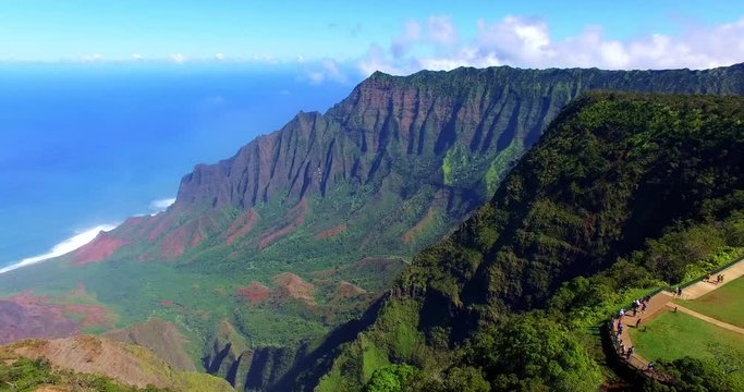 Slow Traveling Aerial of Steep Mountain Ridge with Tourist Overlook of Surrounding Tropical Green Valley framed by Blue Ocean on Coast - Aerial Footage from Kauai, Hawaii