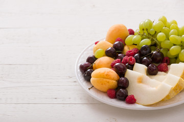 Assortment of juicy fruits on white plate and white table background.. Organic raspberries, apricots, melon, cherries - summer dessert or snack. healthy eating concept.