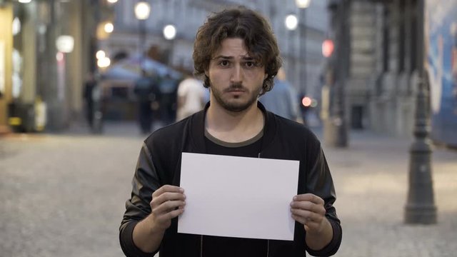 Sad young man holding a white copy space banner on the street