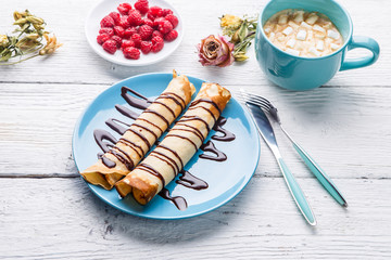 Homemade pancakes or russian blini with chocolate sauce on plate on white wooden background.