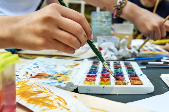 Teen girls painting pictures together. Close up view of their hands holding paintbrushes  