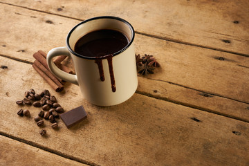 Vintage mug of hot chocolate drink with cinnamon sticks coffee beans anise and piece of chocolate on old wooden rustic table with copy space.