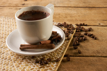 Coffee cup and coffee beans with cinnamon sticks and anise on old rustic wooden table