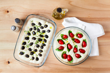 Preparation of focaccia with olives and tomatoes. Raw dough in glass sheet left to leavening on a wooden table