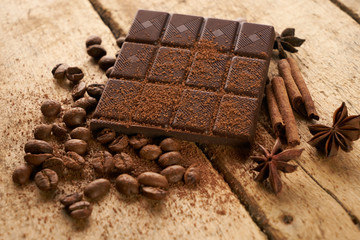 Cinnamon sticks, dark chocolate bar, arabica coffee beans, anise and cocoa powder on wooden old rustic background