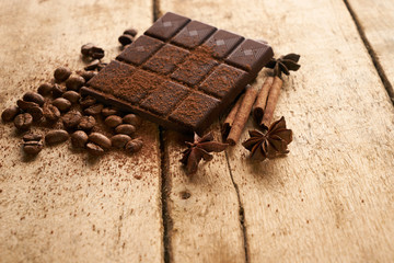A large bar of dark chocolate arabica coffee beans cinnamon and anise on old wooden rustic background with copy space.