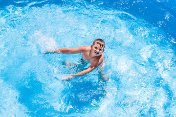 Fototapeta na wymiar Young boy kid child eight years old splashing in swimming pool having fun