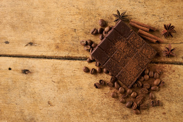 Close-up of roasted arabica coffee beans, dark chocolate bar and spices anise with cinnamon stick and cocoa powder on old rustic wooden background with copy space.