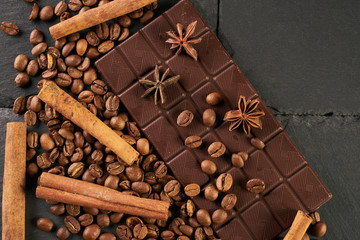 Close-up of roasted arabica coffee beans, dark chocolate bar and spices anise with cinnamon on dark stone background with copy space.
