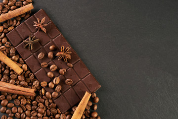 Aromatic set of chocolate bar, arabica coffee beans, anise and cinnamon on dark stone background with copy space