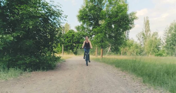 Young beautiful caucasian girl rides a bicycle in the countryside enjoying their healthy lifestyle. Front view. Green meadow, forest and park trail in the background. Travel sport lifestyle concep.