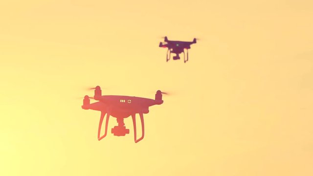 Close up view of two drone quad copters with high resolution digital camera flying aerial in spectacular sunset orange sky. Modern technology. Kiev, Ukraine. Travel, hobby, inspiration. Filter toning