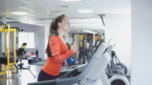 Attractive caucasian girl running on the treadmill in the sport gym, 4k