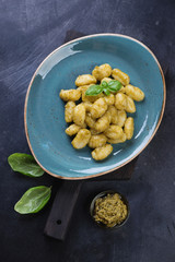 Potato gnocchi served with basil pesto on a turquoise plate, flat-lay on a dark metal background, vertical shot