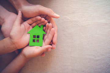 Adult and child hands holding green paper house, eco house concept