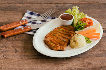 Barbecue pork steak slices on white plate. Delicious pork steak for lunch or dinner on wood table. Moist and soft homemade pork barbecue served with mash potato barbecue sauce and vegetable.