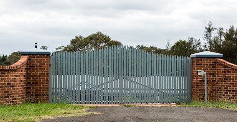 Driveway entrance gates set in brick fence with trees in background