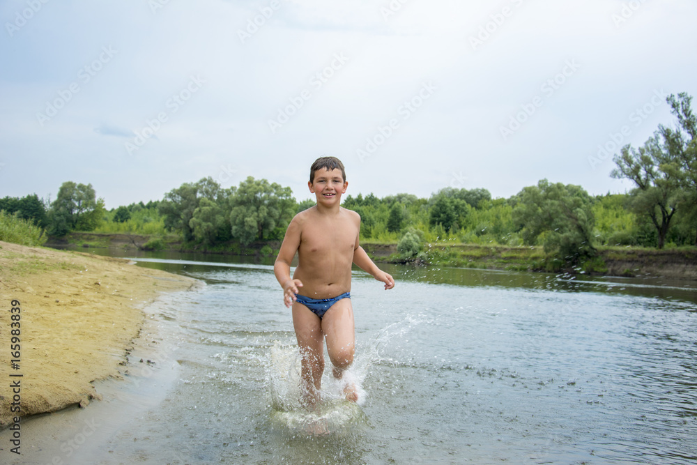 Wall mural in the summer on the river the boy runs along the shore.