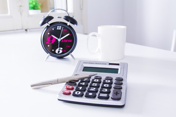 Cup of coffee with woken up clock and calculator in the office