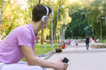 young men waiting date holding mobile phone sitting on a bench and listening music