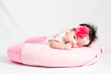 Portrait of a little adorable infant baby girl lying on the tummy on the pillow with head band